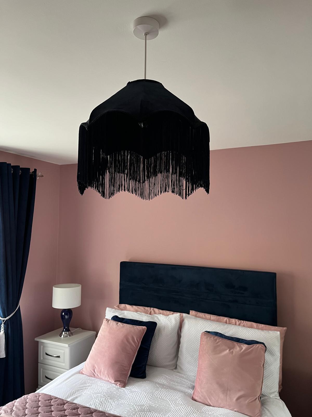 a pink bedroom with a navy fringed ceiling shade, navy bed, with pink and navy throw cushions. Side lamps have navy bases and white shades.